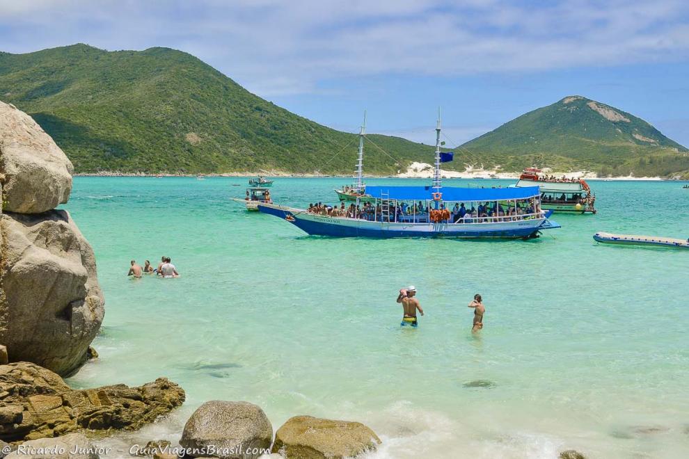 Imagem de um barco chegando repleta de turistas na Praia do Pontal do Atalaia.